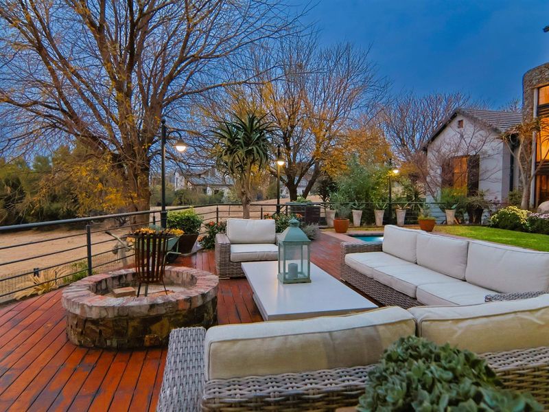 Spacious outdoor timber deck featuring a built-in brick fire pit, metal safety railings, and ambient lighting, overlooking the garden and pool area.