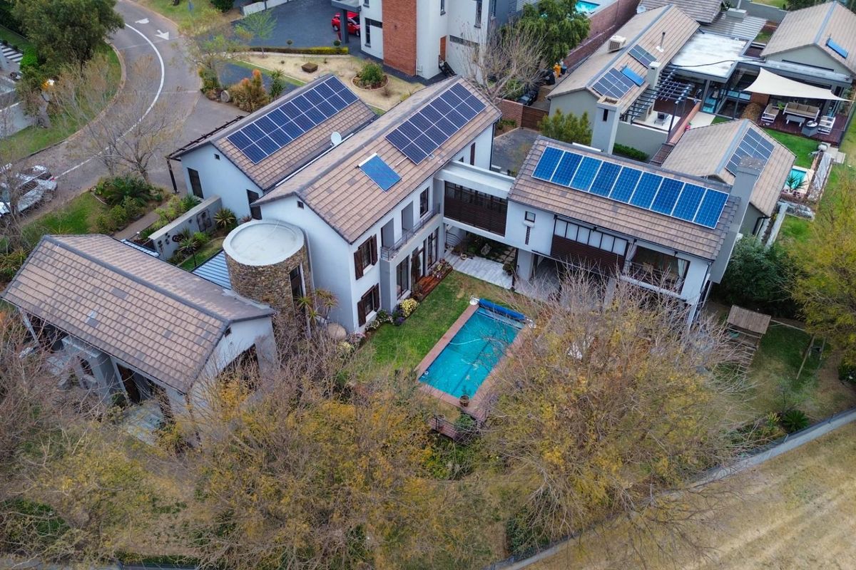 Aerial view of a residential property featuring multiple roof-mounted solar panel arrays, a private swimming pool, and landscaped garden areas.