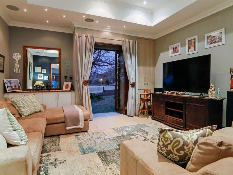A comfortable living room featuring a tray ceiling with recessed lighting, built-in cabinetry, tiled floors, and double glass doors leading to the garden.