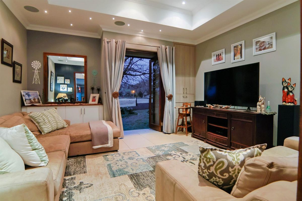 A comfortable living room featuring a tray ceiling with recessed lighting, built-in cabinetry, tiled floors, and double glass doors leading to the garden.