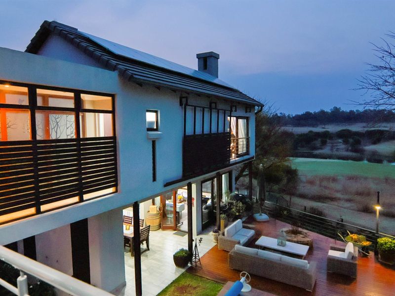 Rear elevation of a two-story residence featuring a spacious timber deck, balcony, and large sliding glass doors overlooking a scenic landscape.
