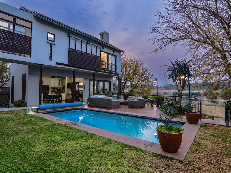Rear exterior view of a two-story house featuring a swimming pool, wooden decking, and a balcony overlooking a scenic landscape.