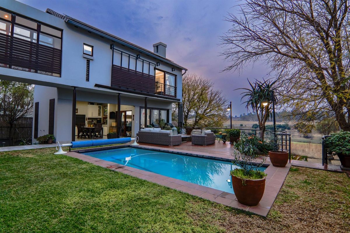 Rear exterior view of a two-story house featuring a swimming pool, wooden decking, and a balcony overlooking a scenic landscape.