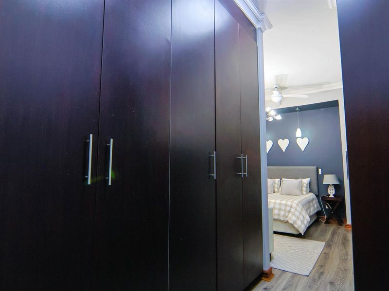 A bedroom featuring dark wood built-in cupboards, laminate flooring, and a ceiling fan, leading into a well-lit sleeping area.