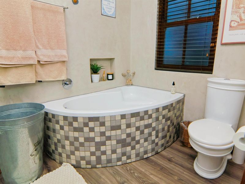 A bathroom featuring a built-in corner bathtub with mosaic tile detailing, a toilet, and a recessed wall niche for storage.