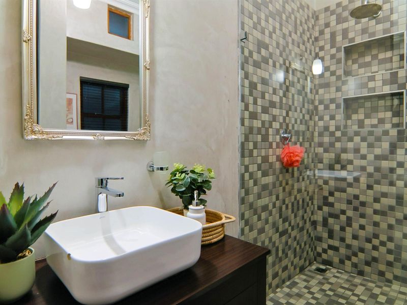 Modern bathroom featuring a vessel sink on a dark vanity cabinet and a walk-in shower with mosaic tiling and a built-in niche.