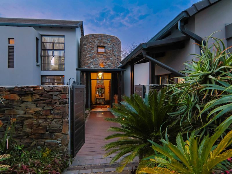A striking modern entrance featuring a unique stone-clad circular tower, timber walkway, and landscaped garden, creating a sophisticated and welcoming facade.