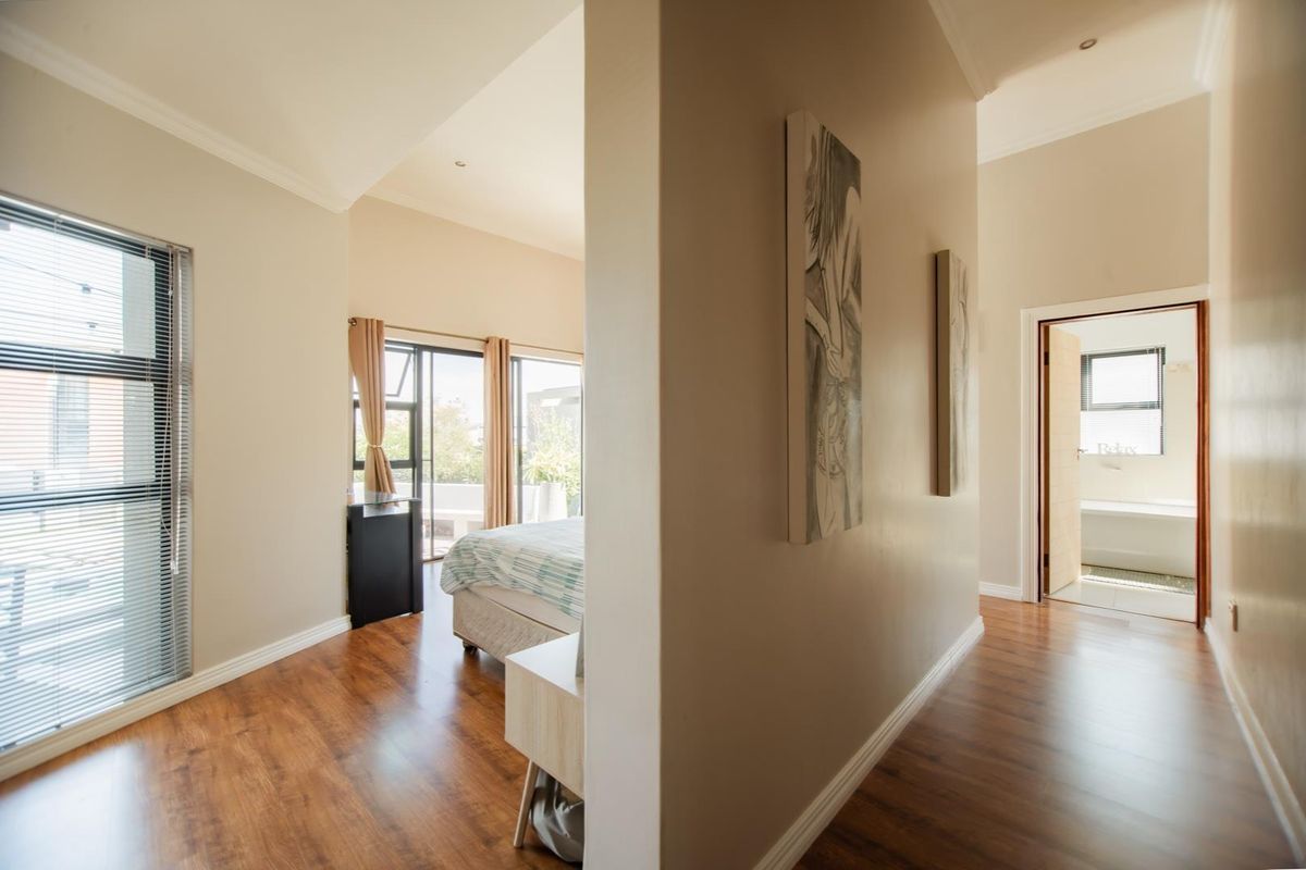 A spacious bedroom featuring warm wood-look flooring, high ceilings, and direct access to an outdoor balcony, with an adjoining en-suite bathroom visible.