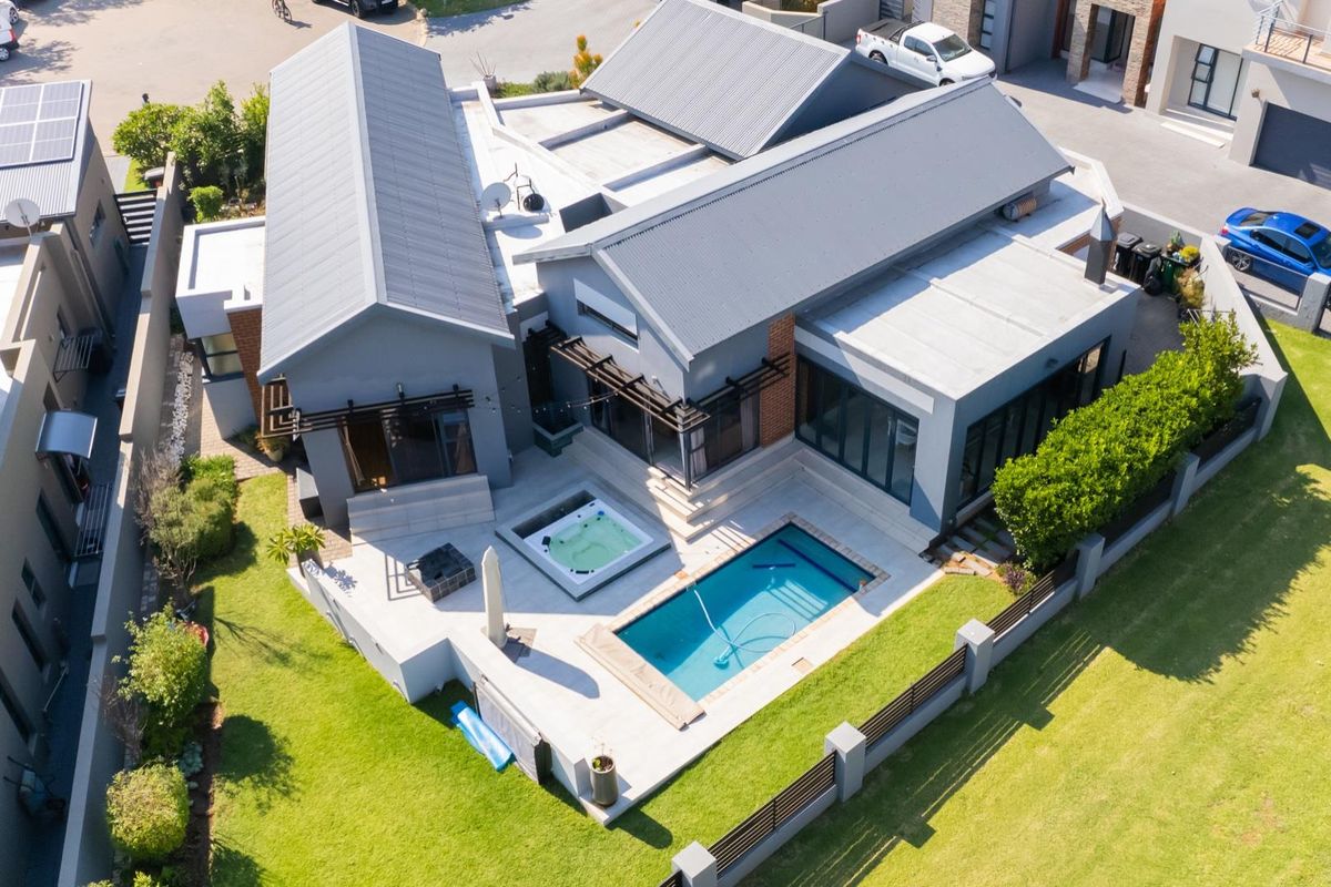 Aerial view of a modern residential property featuring a swimming pool, integrated spa, paved patio area, and landscaped garden.