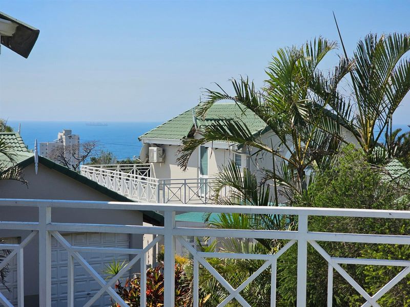 An elevated view of the townhouse exterior featuring a balcony railing, tiled roof, and a scenic ocean backdrop.