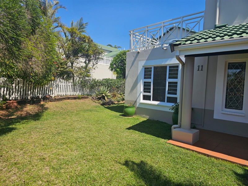 A well-maintained townhouse exterior featuring a front garden, tiled patio, and an upper-level balcony with white railings.