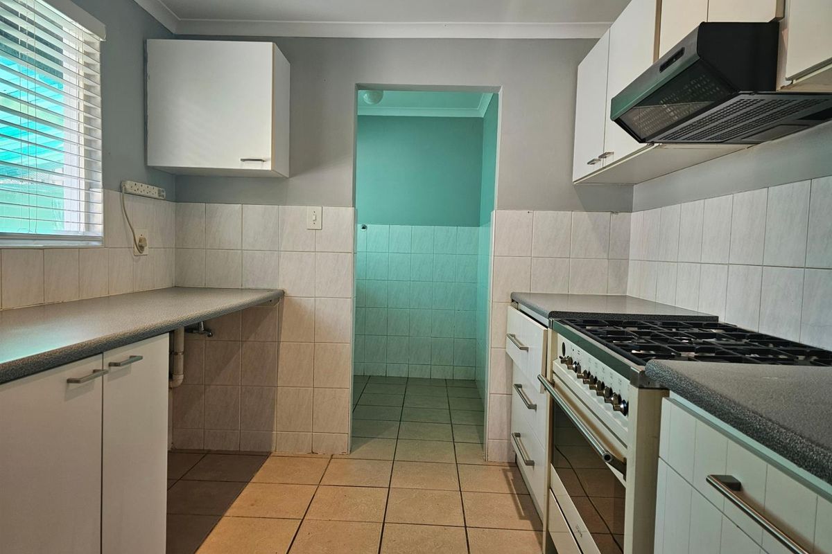Functional kitchen featuring built-in cabinetry, gas stove with extractor fan, tiled splashbacks, and direct access to a secondary utility or scullery area.