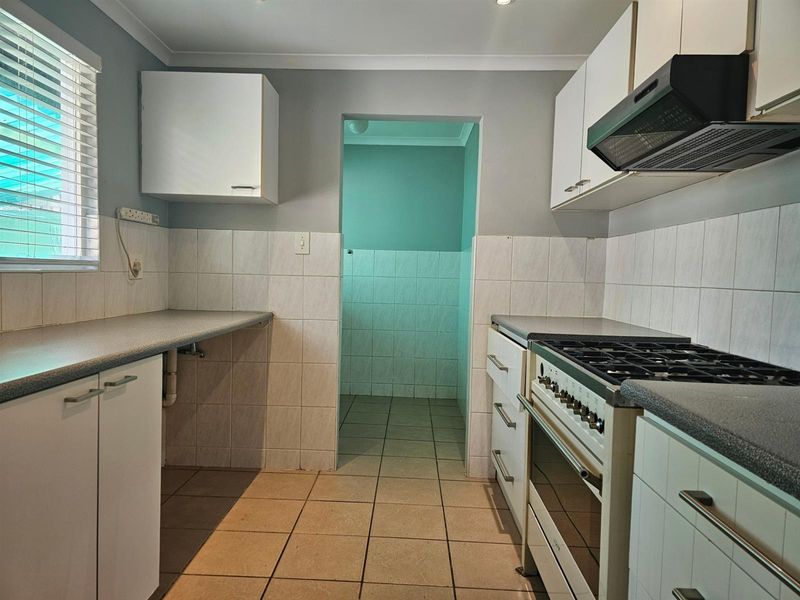 Functional kitchen featuring built-in cabinetry, gas stove with extractor fan, tiled splashbacks, and direct access to a secondary utility or scullery area.