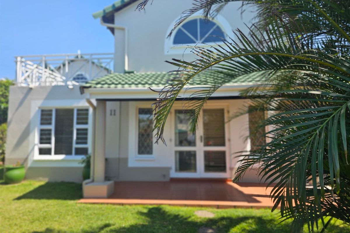 Rear view of the townhouse featuring a covered tiled patio, upper-level balcony, and well-maintained garden area.