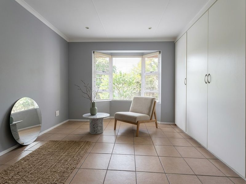 A bright bedroom featuring neutral grey walls, tiled flooring, built-in cupboards, and a large bay window that allows for ample natural light.