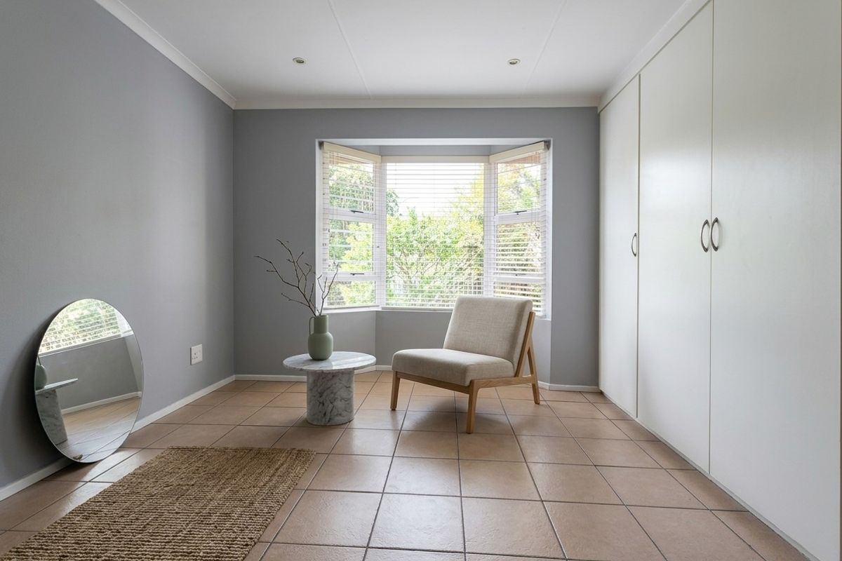 A bright bedroom featuring neutral grey walls, tiled flooring, built-in cupboards, and a large bay window that allows for ample natural light.