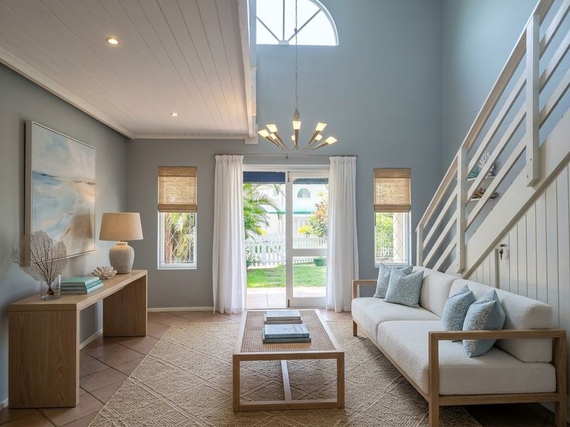 Bright living room featuring a double-volume vaulted ceiling, staircase with timber balustrade, and sliding glass doors opening to a rear garden.