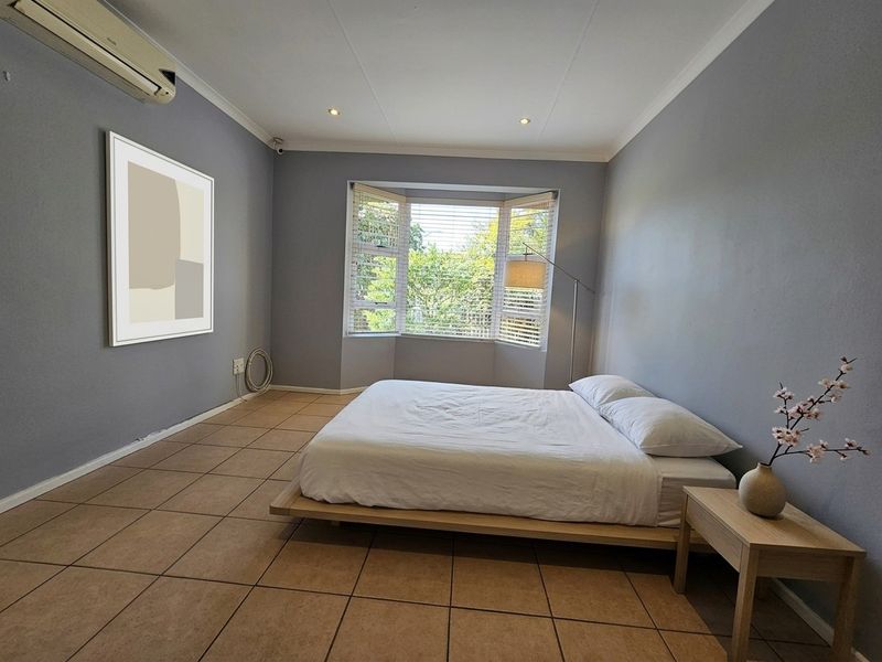 Spacious bedroom featuring tiled flooring, a bay window with blinds, and a wall-mounted split-system air conditioner.
