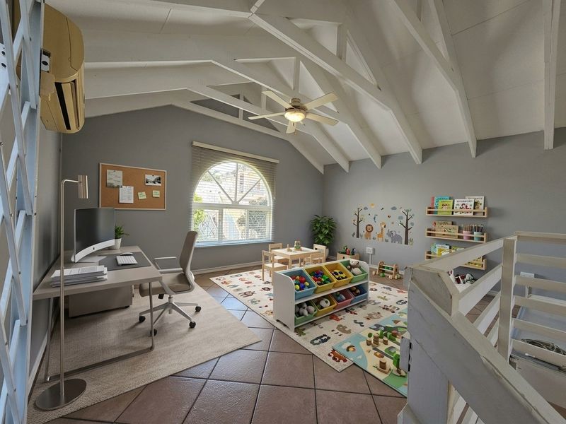 A spacious loft-style office featuring vaulted ceilings with exposed rafters, tiled flooring, an arched window, and a wall-mounted air conditioning unit.