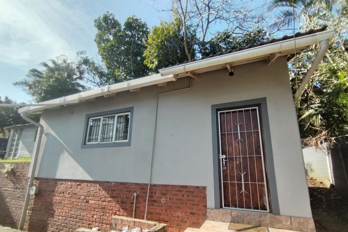 Exterior view of the guest house featuring a brick base, plastered walls, security gate, and guttering system.