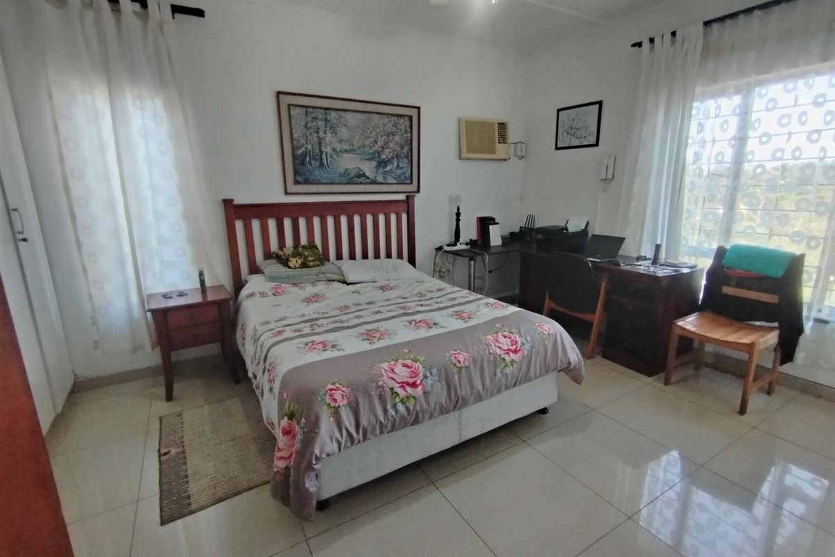 A functional bedroom featuring tiled flooring, dual windows with curtains, a ceiling fan, and a wall-mounted air conditioning unit.