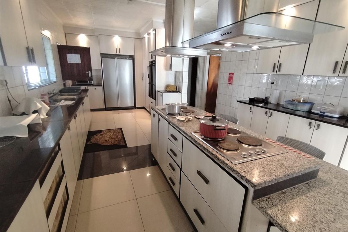 A spacious, modern kitchen featuring a central island with a built-in hob, stainless steel extractor fan, granite countertops, and ample white cabinetry.