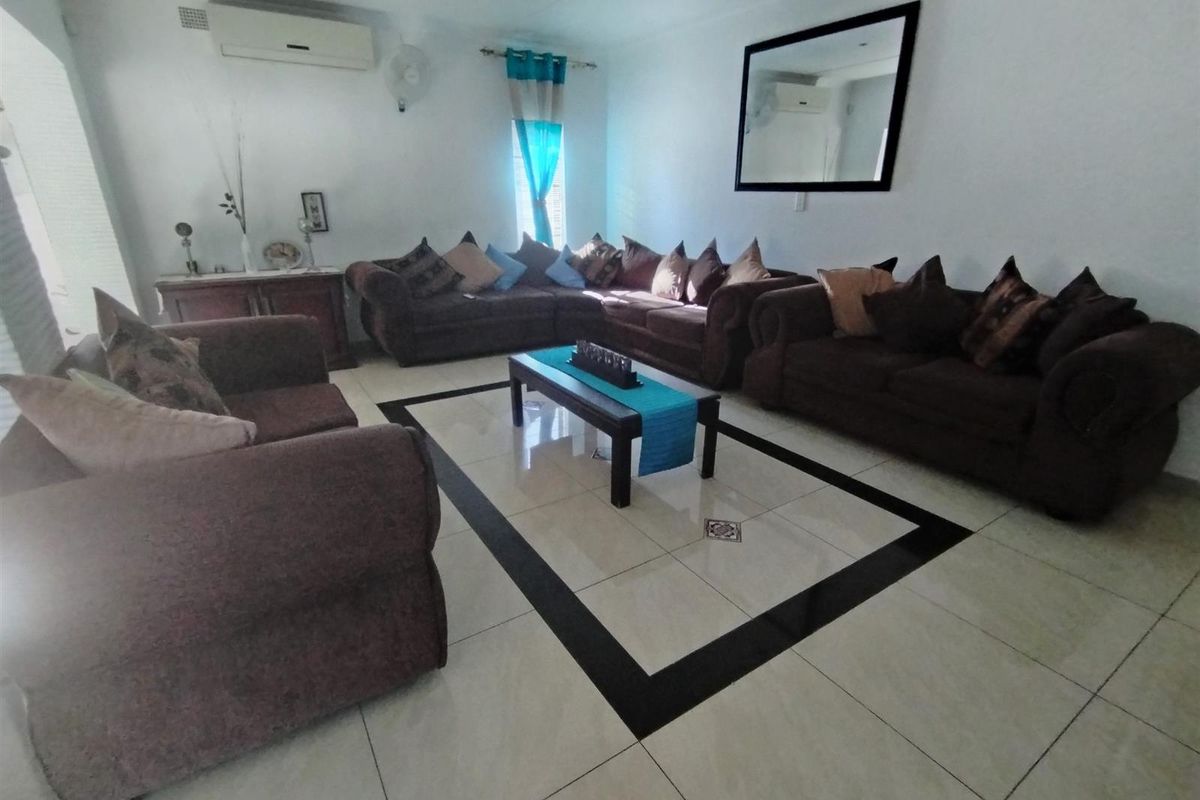 A spacious living room featuring large format tiled flooring with a decorative border, wall-mounted air conditioning unit, and recessed ceiling lighting.