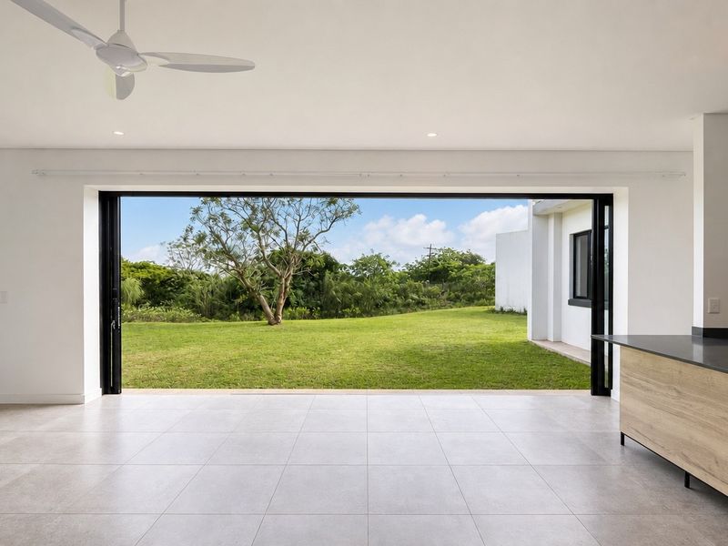 Spacious open-plan living area featuring large sliding glass doors that open to a private garden, complemented by modern tiled flooring and a kitchen island.