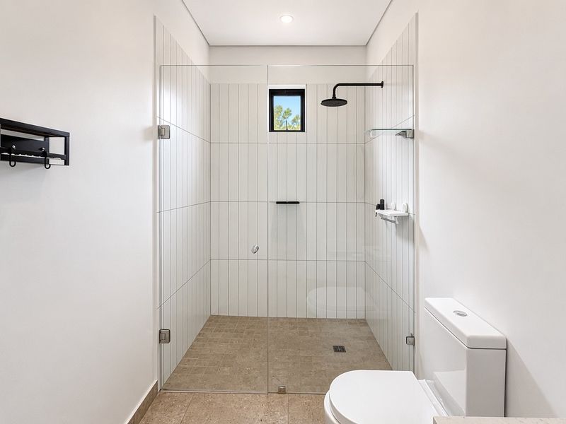 Modern bathroom featuring a walk-in shower with a glass screen, rain shower head, vertical wall tiling, and a wall-mounted toilet.