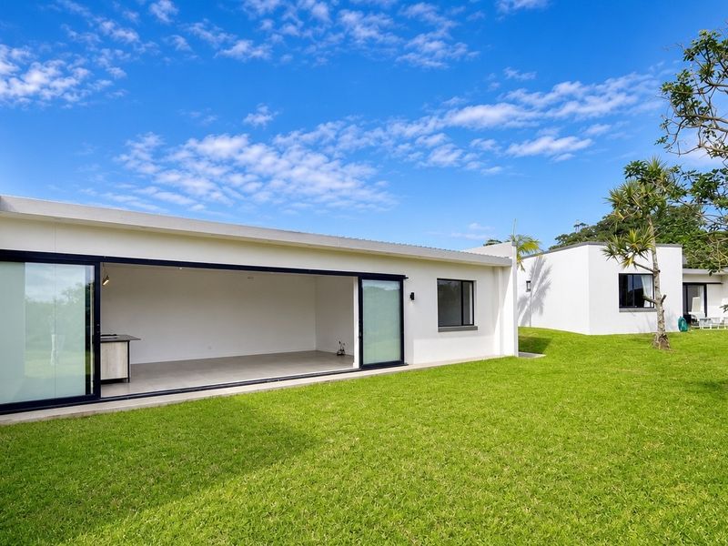 A modern townhouse exterior featuring a spacious rear lawn and large sliding glass doors opening into an open-plan living area.