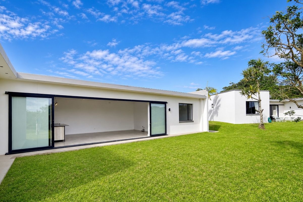A modern townhouse exterior featuring a spacious rear lawn and large sliding glass doors opening into an open-plan living area.
