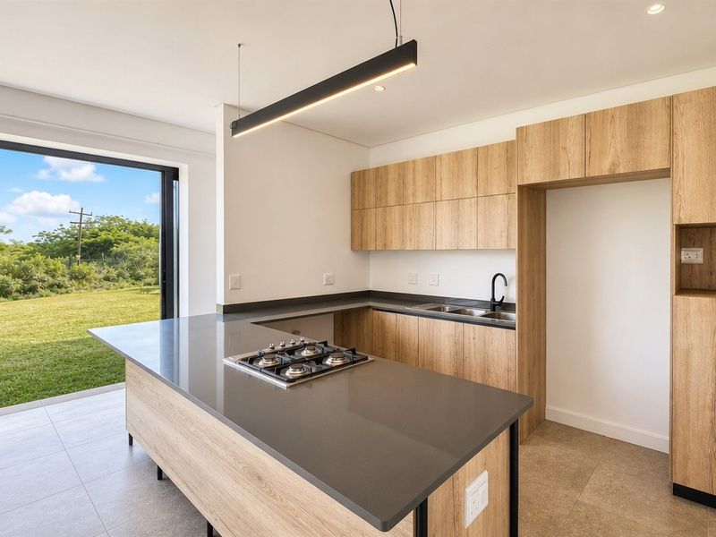 Modern kitchen featuring light wood cabinetry, stone countertops, a central gas hob, and direct access to the garden through large sliding glass doors.