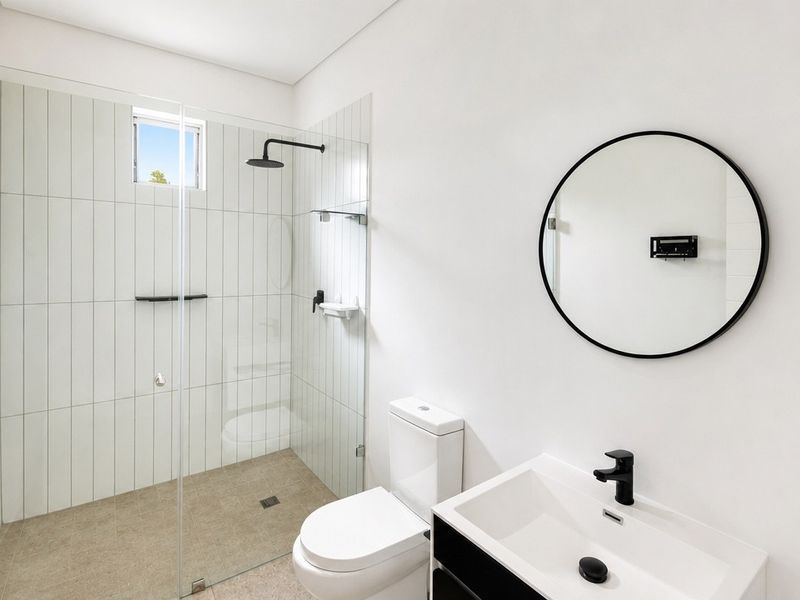 Modern bathroom featuring a walk-in shower with glass screen, black matte fixtures, wall-mounted toilet, and a sleek vanity basin.