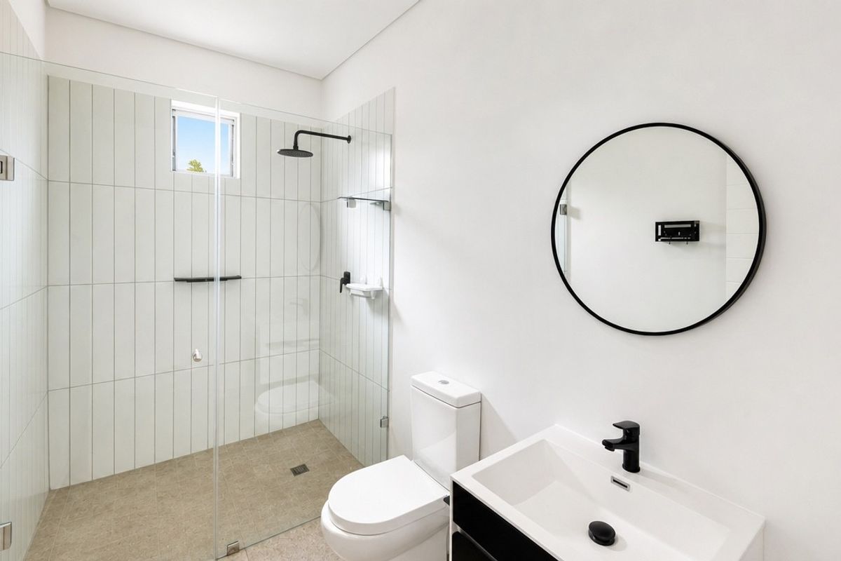 Modern bathroom featuring a walk-in shower with glass screen, black matte fixtures, wall-mounted toilet, and a sleek vanity basin.