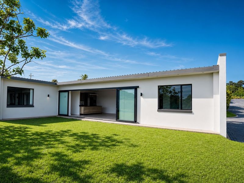 A well-maintained rear exterior view of the townhouse featuring a spacious lawn, paved driveway, and large sliding glass doors leading to the interior.