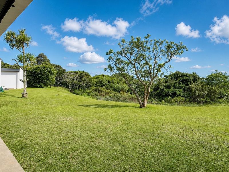 A spacious, well-maintained lawn area extending from a modern townhouse, featuring a tiled patio and expansive views of the surrounding greenery.