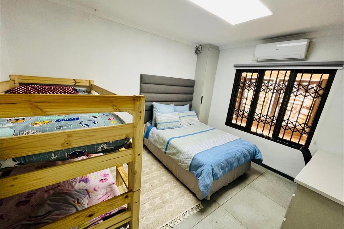 A functional bedroom featuring tiled flooring, a wall-mounted air conditioning unit, and security bars on the window.