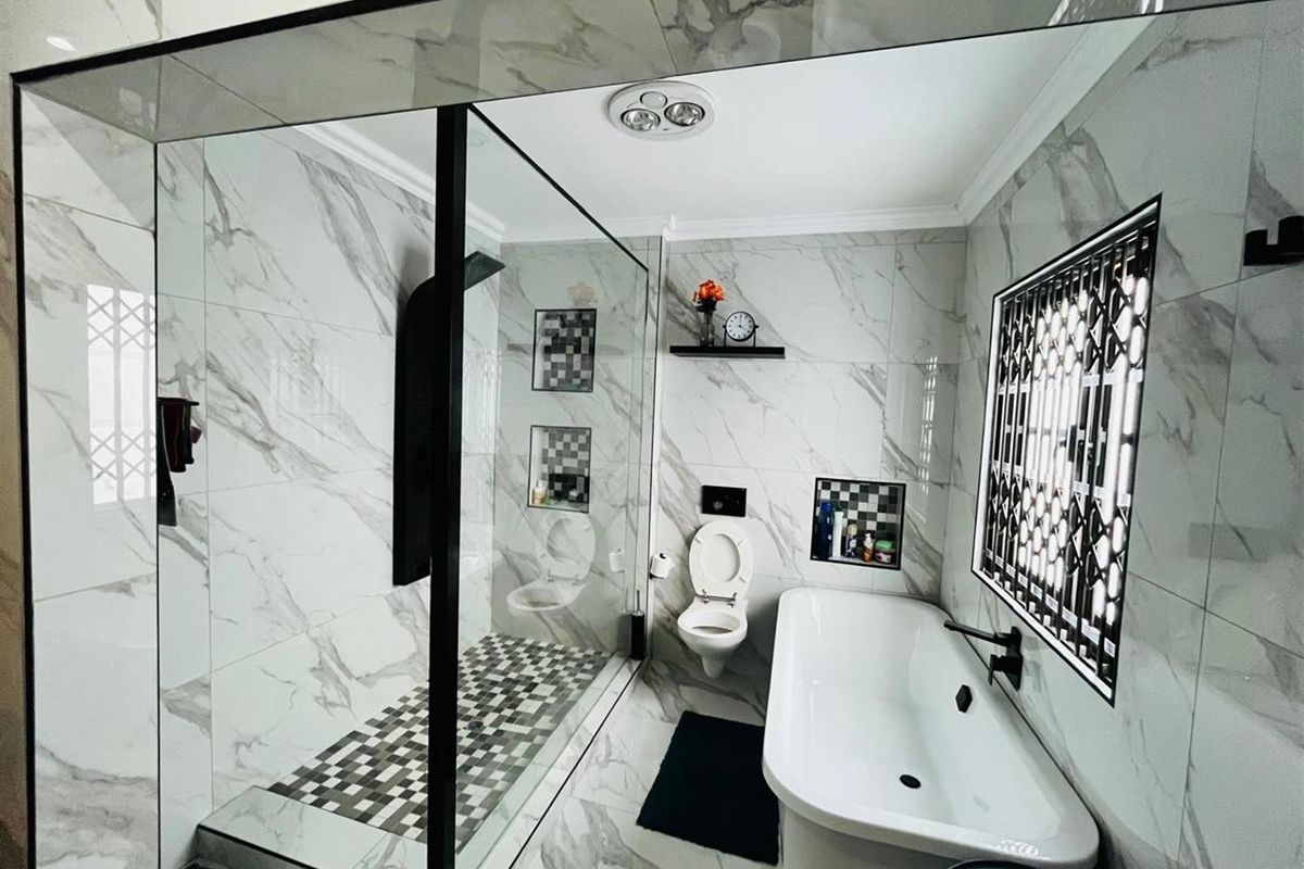 Modern bathroom featuring floor-to-ceiling marble-look tiling, a glass-enclosed walk-in shower, a freestanding bathtub, and a wall-mounted toilet.