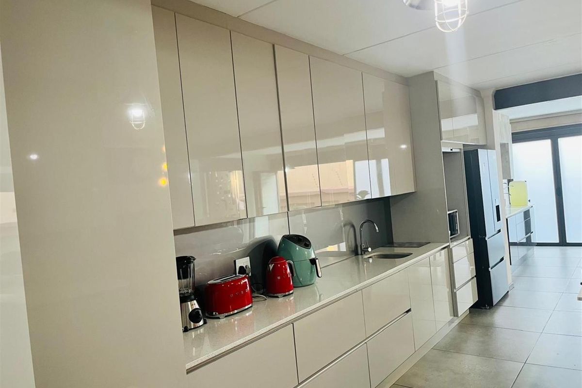 Modern kitchen featuring sleek high-gloss cabinetry, stone countertops, integrated sink, and clean tiled flooring in a contemporary open-plan layout.
