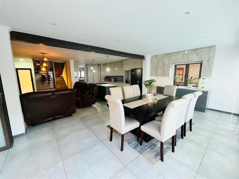Spacious open-plan living and dining area featuring large format floor tiles, a modern kitchen with integrated cabinetry, and a prominent structural ceiling beam.