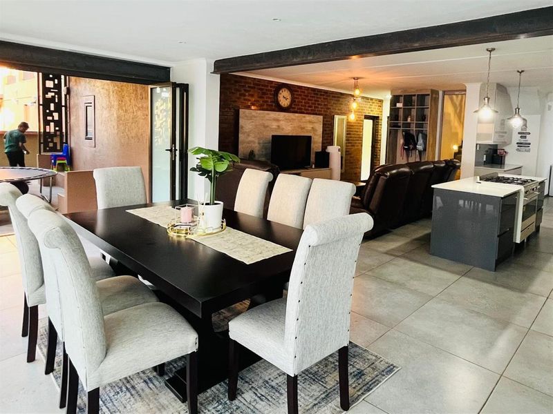 Spacious open-plan living and dining area featuring a modern kitchen with a gas hob, exposed brick feature wall, and large format floor tiles.