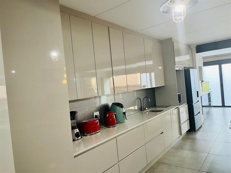 Modern kitchen featuring sleek high-gloss cabinetry, stone countertops, integrated sink, and clean tiled flooring in a contemporary open-plan layout.