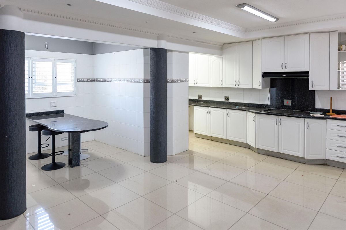 Spacious kitchen featuring white cabinetry, dark granite countertops, a breakfast bar, and tiled flooring with structural columns.