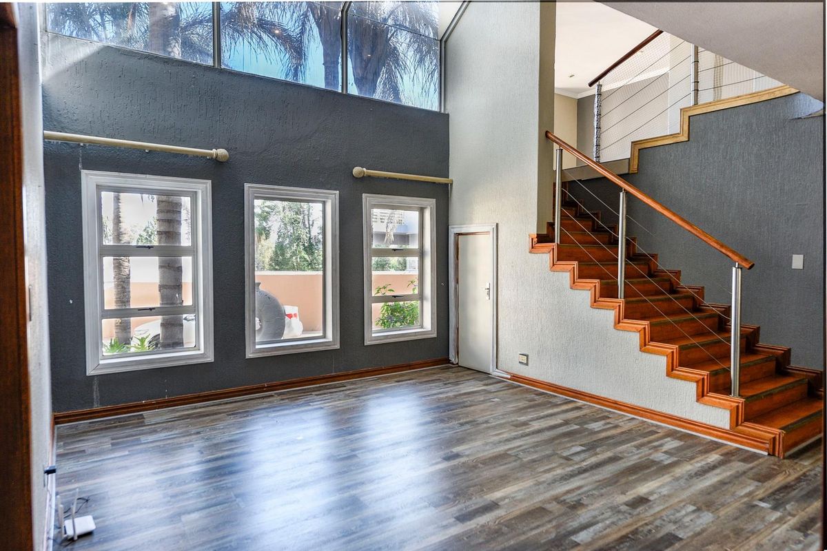 Spacious double-volume living area featuring modern laminate flooring, a timber staircase with stainless steel balustrades, and large windows providing ample natural light.