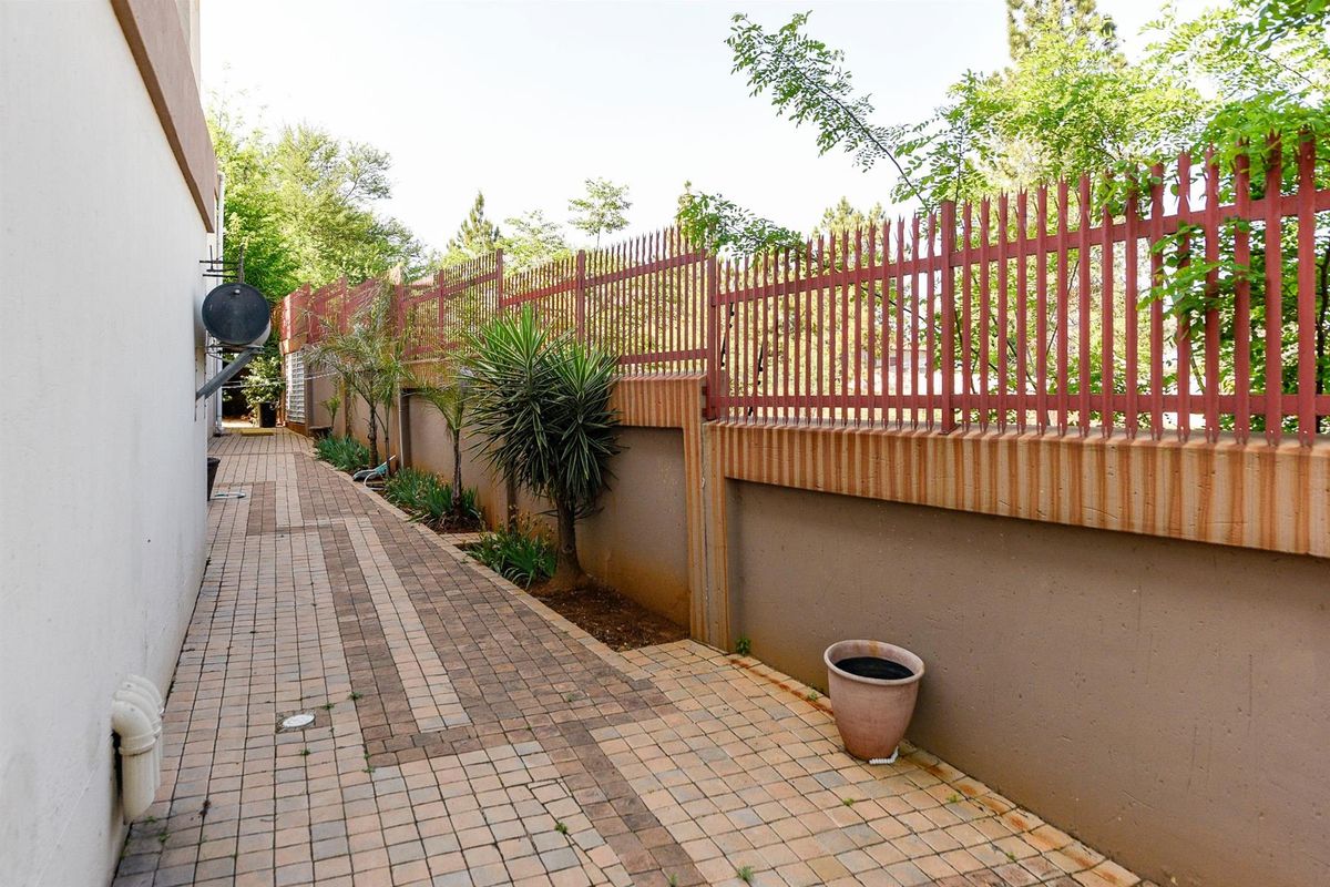 A paved side walkway featuring a high perimeter wall with integrated metal security fencing and established garden border.