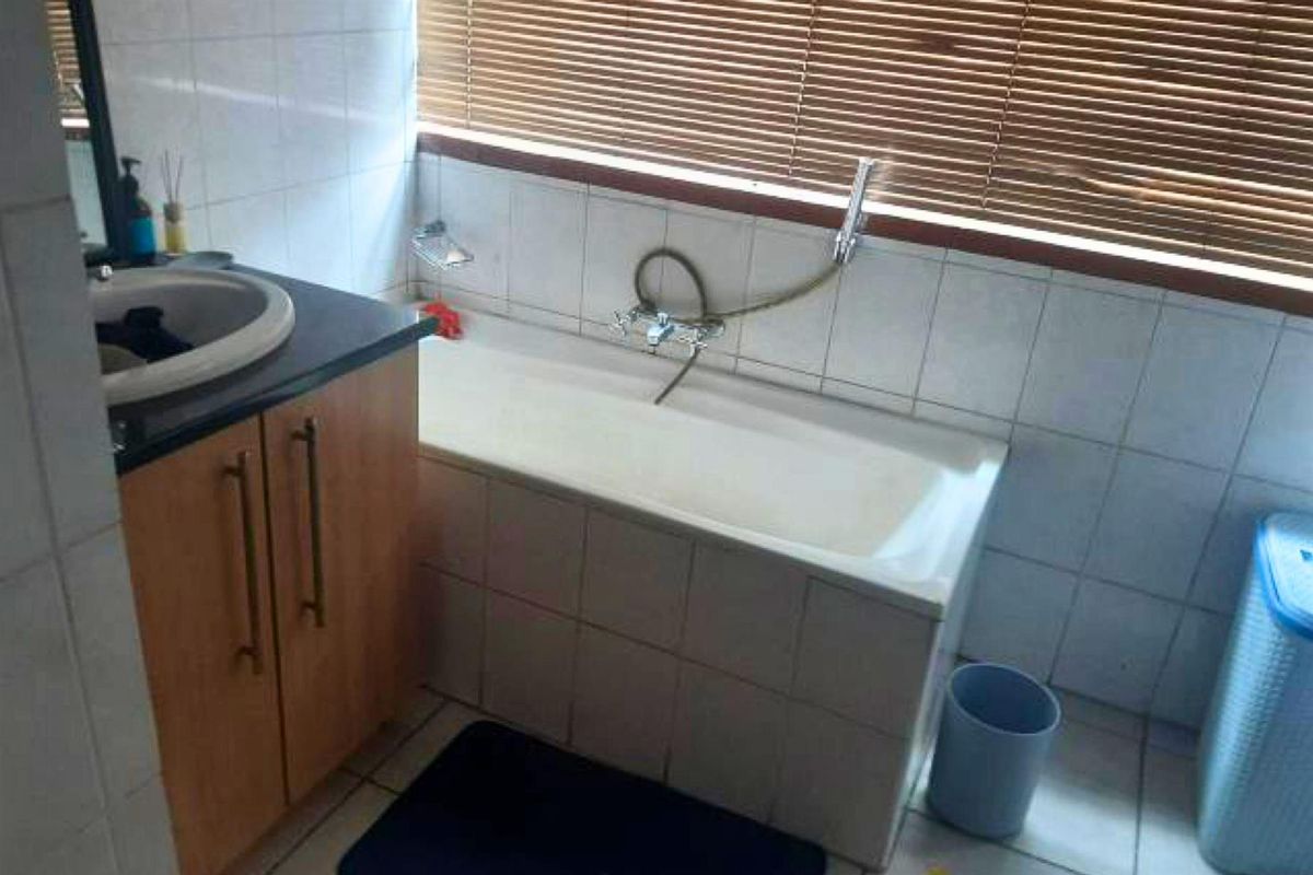 A functional bathroom featuring a built-in bathtub with shower attachment, tiled walls, and a vanity cabinet with a basin.