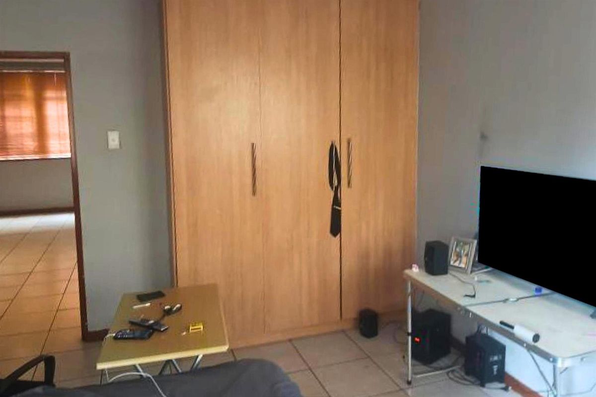 A bedroom featuring built-in wooden cupboards and tiled flooring, with an adjacent hallway visible.