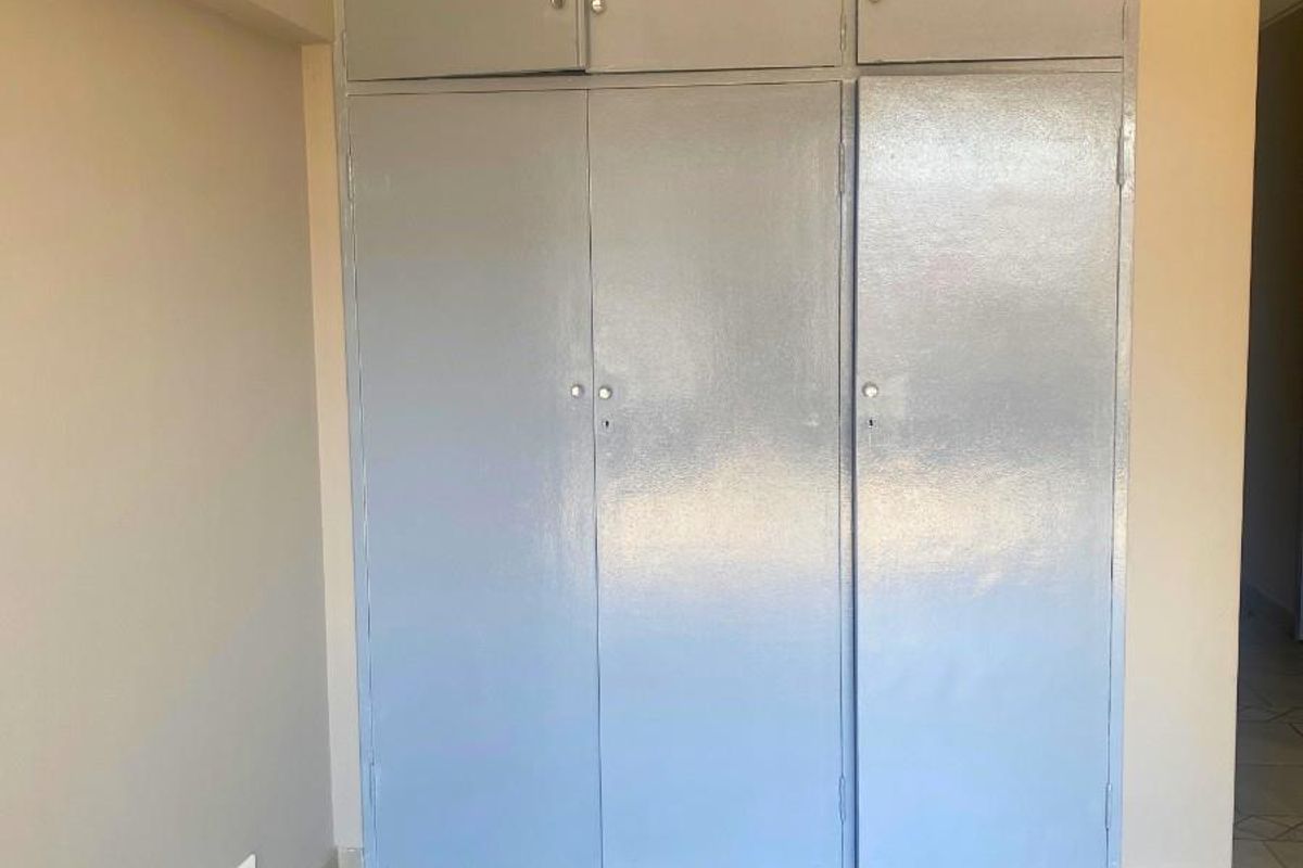 A bedroom interior featuring built-in floor-to-ceiling storage cupboards with a neutral tiled floor finish.