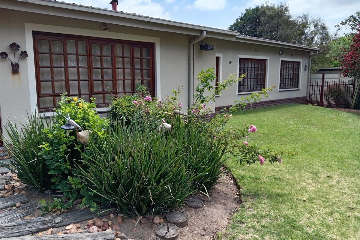 A view of the rear exterior of the house, featuring a landscaped garden bed, lawn, and timber-framed windows.