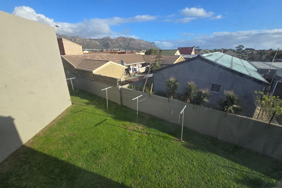An elevated view of a private backyard featuring a grass lawn and perimeter boundary walls, set against a mountain backdrop.